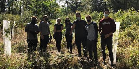 Group of volunteers with masks on standing next to tree protectors
